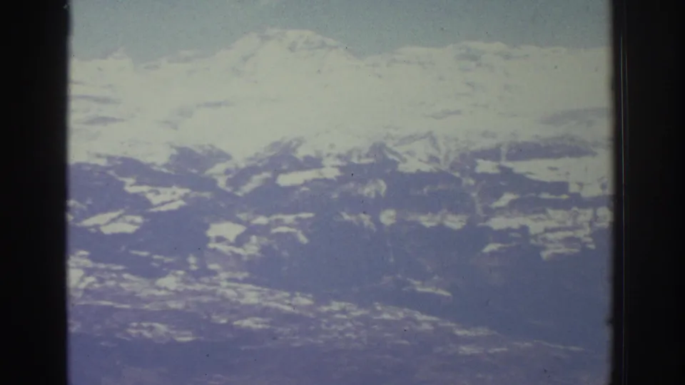 Panoramic view of snow-covered alpine peaks filmed from a moving vehicle, likely Swiss Alps circa 1976, with characteristic 8mm film grain and color aging.