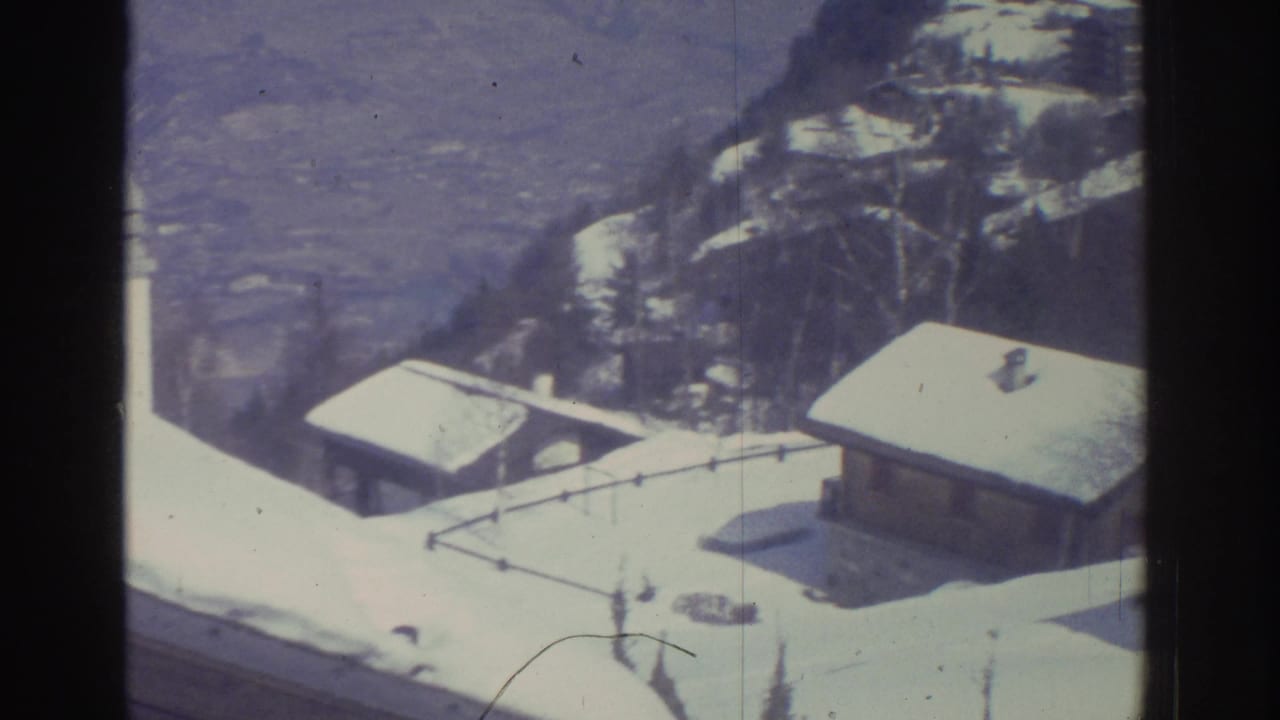 Bird's-eye view of snow-covered alpine rooftops and buildings on a hillside, shot on 8mm film.