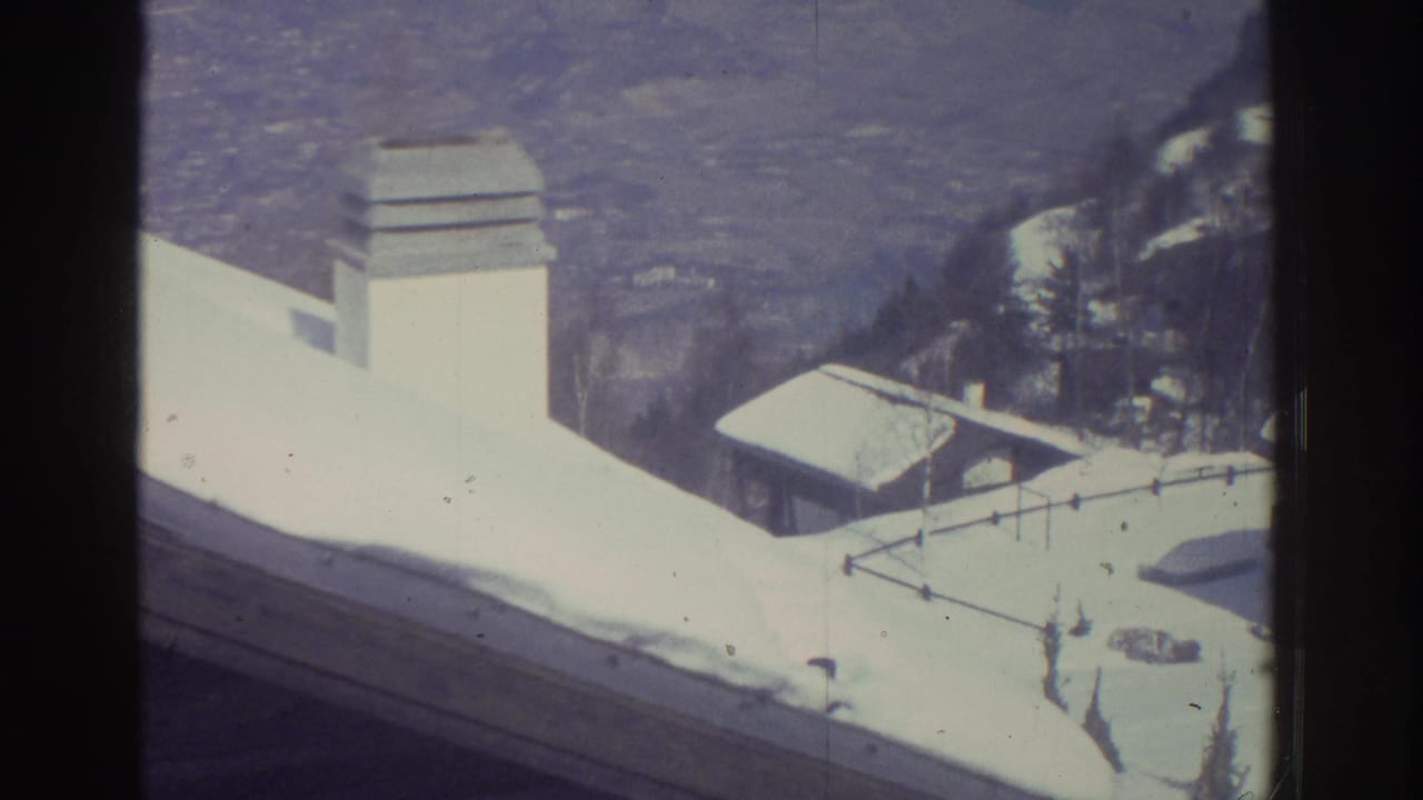 8mm home-movie view from a rooftop looking across snow-laden slopes and a chimney stack toward lower alpine buildings and valley; attributed to Bern, Switzerland, 1976.
