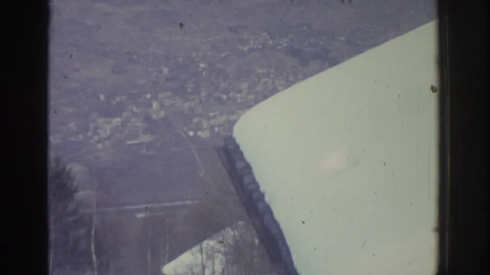 Final frame of 8mm pan showing snow-covered rooftop foreground and a broad snowy valley floor with distant structures; attributed to Bern, Switzerland, 1976.