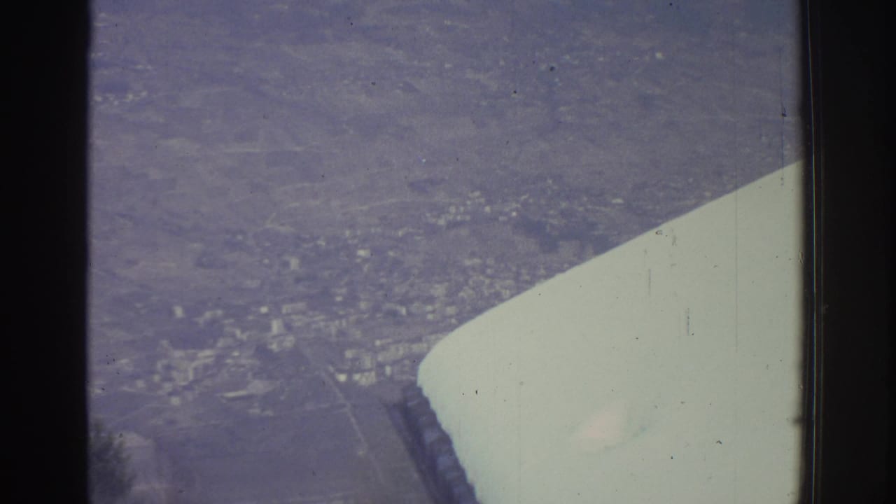 Continuation of 8mm aerial sequence circa 1976, airplane wing visible at right, snow-covered town spread across the valley below.