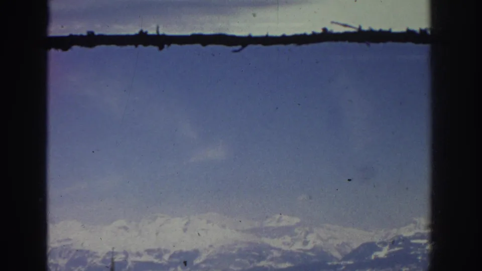 Wide blue sky and distant Swiss alpine ridge at end of a slow pan, chalets no longer centered, mid-1970s 8mm home movie.