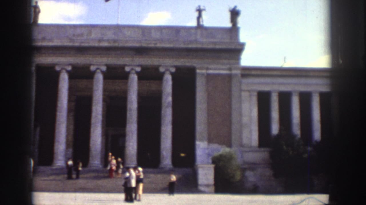 Neoclassical building with tall colonnade; small groups of 1970s-dressed visitors on the steps and forecourt platform.