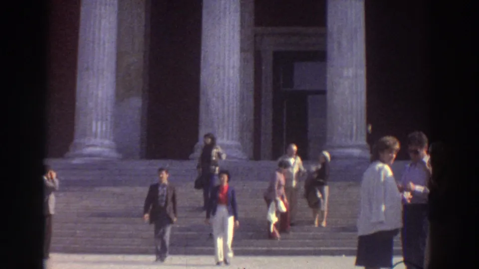 1976 Greece — close-medium 8mm view of visitors in 1970s dress descending wide stone steps beneath towering classical columns of a neoclassical public building.
