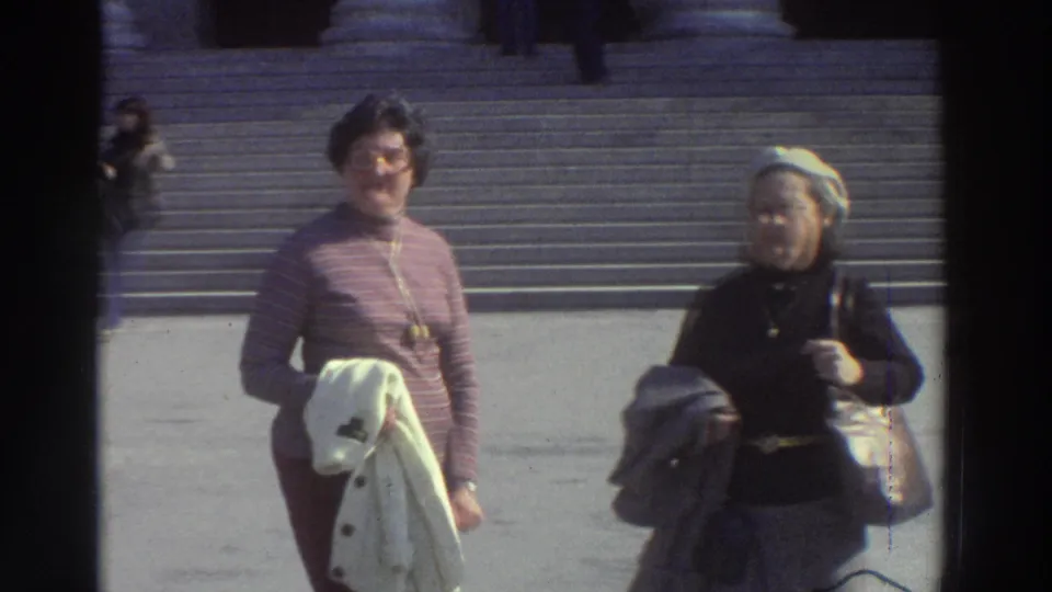 Close view of two women tourists on stone steps at a neoclassical building, Greece, 1976; pink turtleneck and white beret prominent, wristwatch visible.