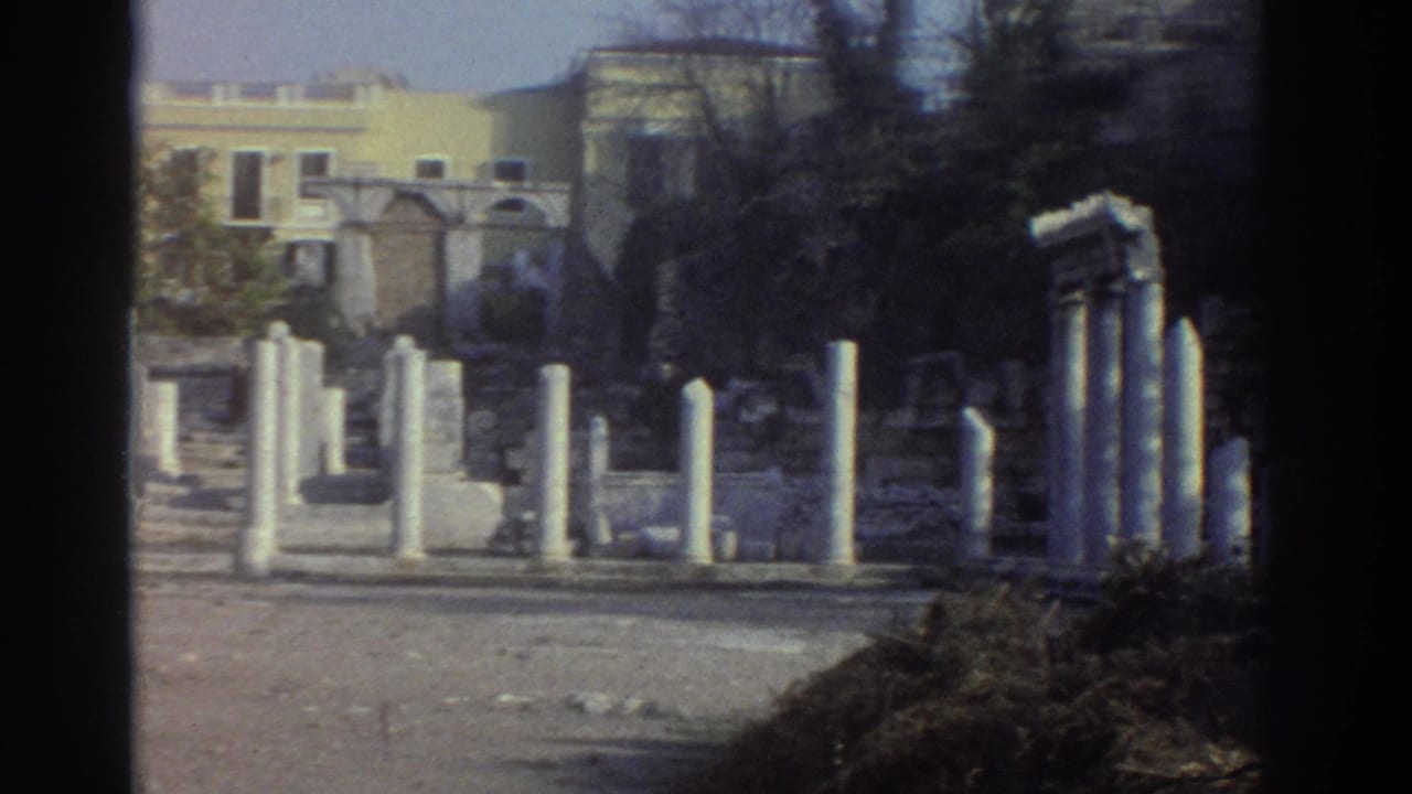 Wide establishing shot of Greek archaeological ruins, mid-1970s 8mm; white marble column remnants and stone rubble under clear sky.