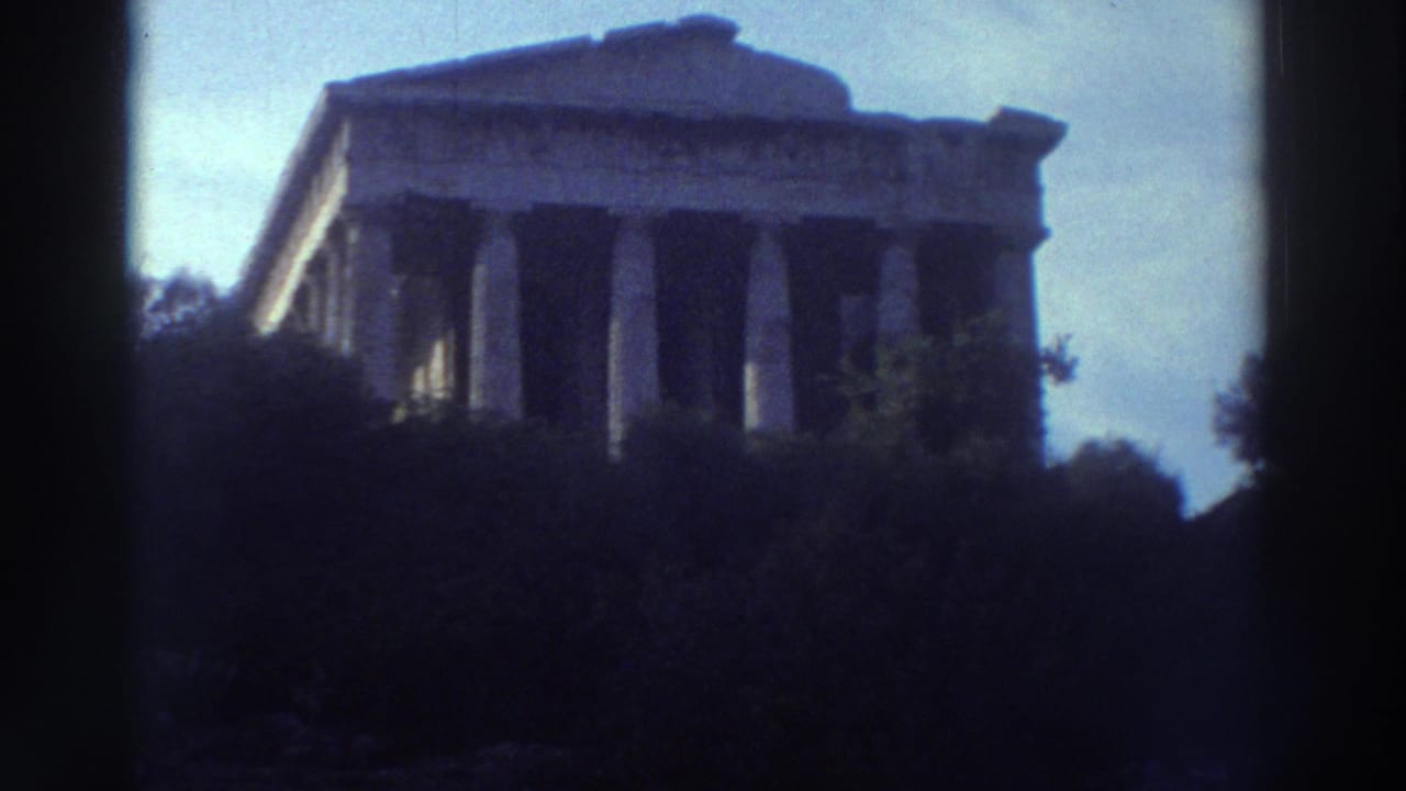 Classical Greek temple with Doric columns seen from below, partially framed by dark trees against a pale blue sky