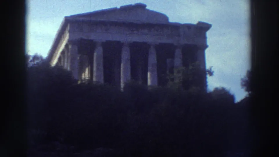 Doric-columned ancient Greek temple shot from low angle with trees in foreground, 8mm home movie footage circa 1976