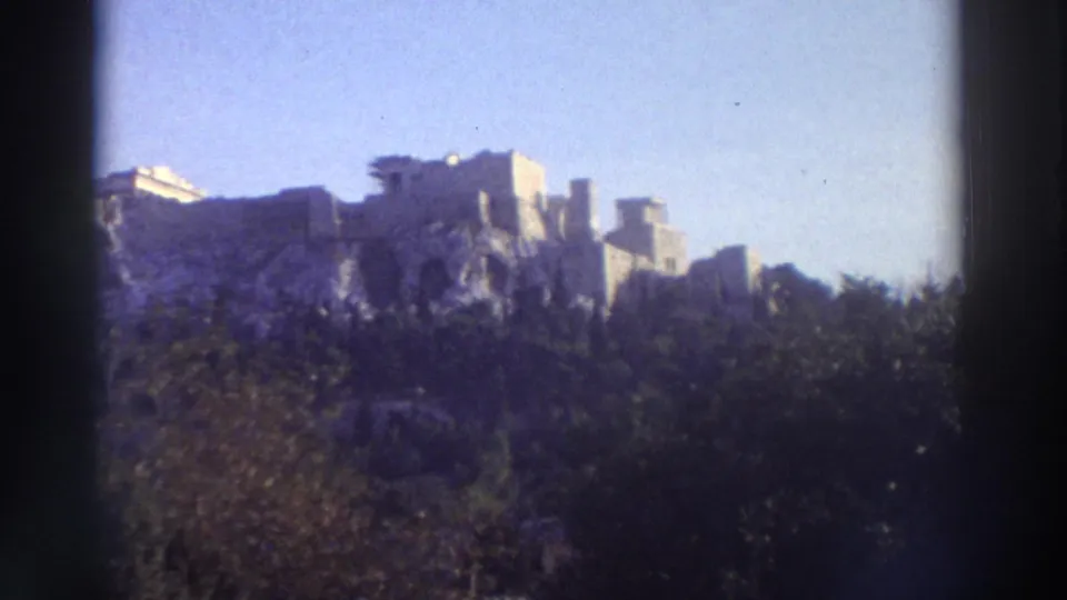 Wide 8mm shot of the Acropolis ruins rising above green hillside vegetation, Athens, Greece, circa 1976.