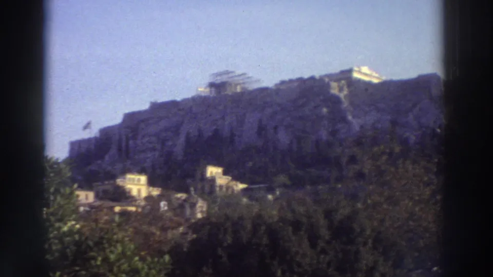 8mm shot of the Acropolis with ruins, surrounding buildings, and what may be a small flag near the summit, Athens, Greece, circa 1976.