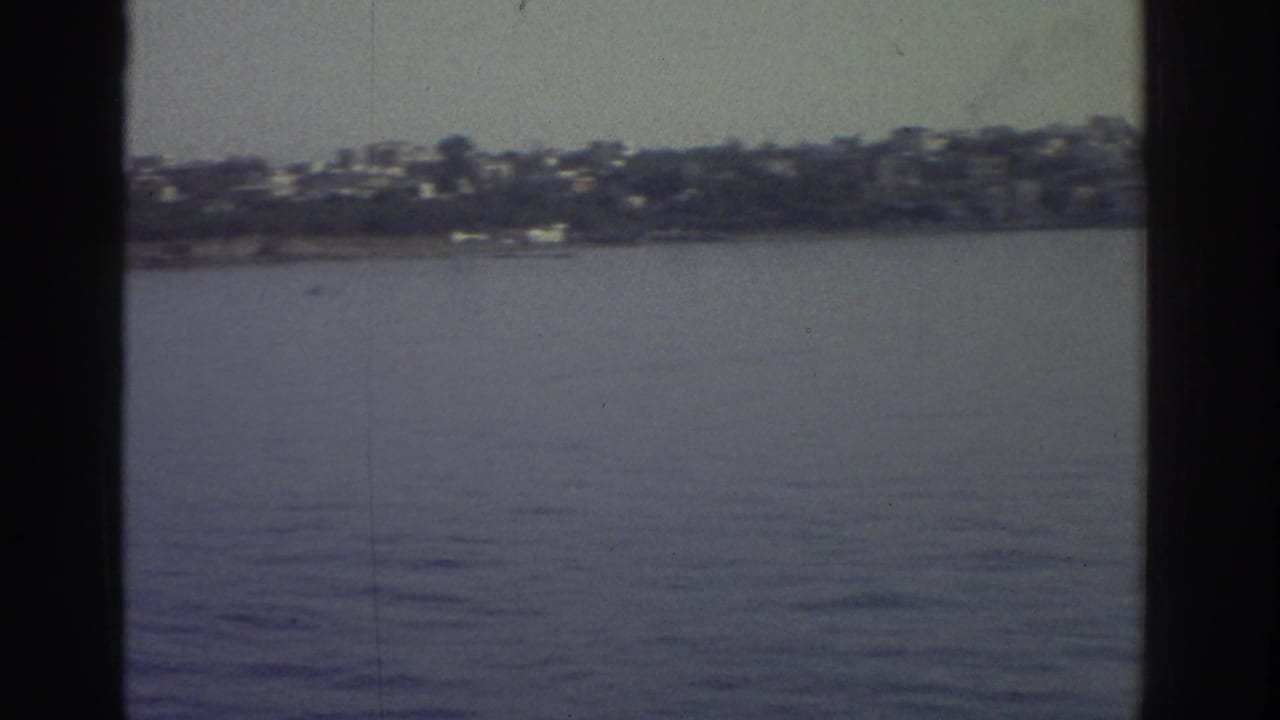 1976 Greece — continued pan across a hillside settlement of white and light-coloured buildings above a calm Mediterranean shoreline; 8mm home movie.