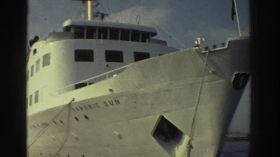The passenger ship 'Saronic Sun' — white hull, multi-deck superstructure, bridge and flag visible — photographed from a nearby vessel, c.1976 Greece.