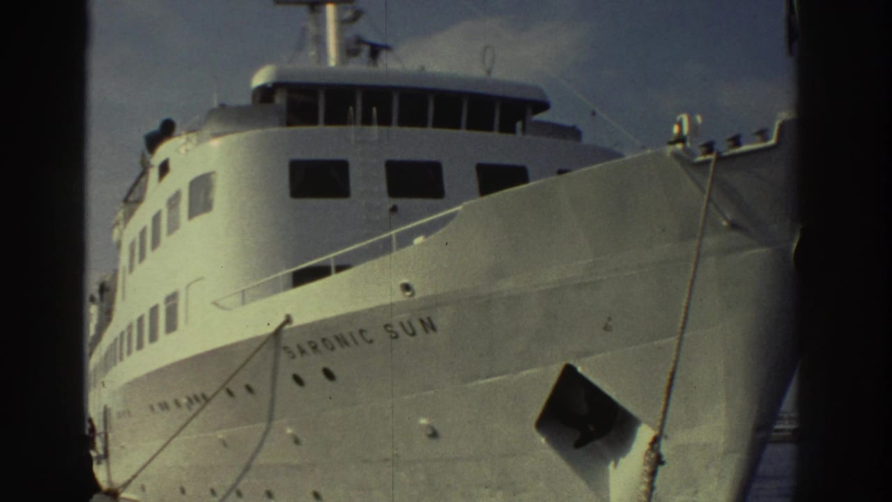 Low-angle 8mm shot of the white cruise ship Saronic Sun moored at a Greek port, circa 1976, hull name clearly legible.