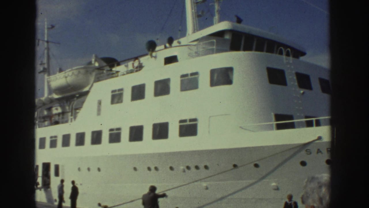 Close-up of the upper decks and superstructure of a large white multi-deck passenger vessel at a Greek port circa 1976; letters beginning 'SAR' are partially legible on the hull.