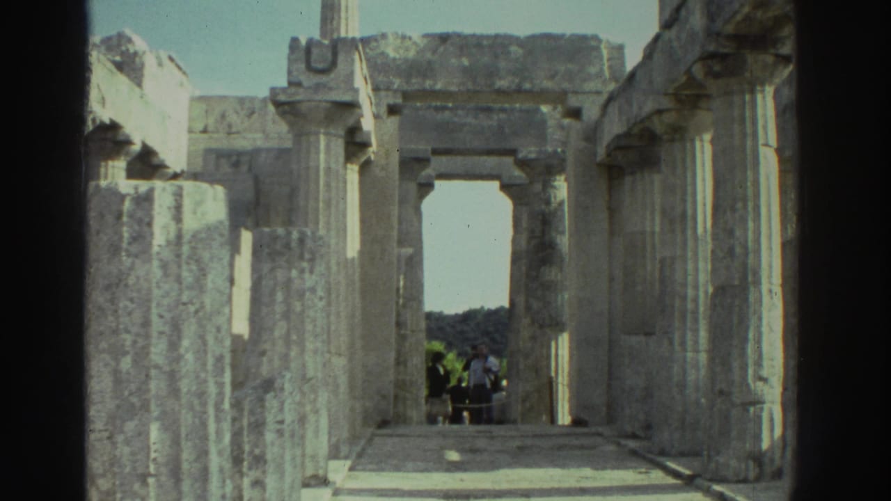 Interior of an ancient Greek stone structure looking through a rectangular doorway toward distant hills and sky, visitors visible in the right background.