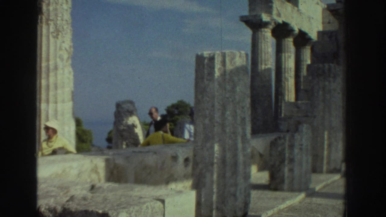 Doric stone columns at an ancient Greek ruin with tourists resting on stone steps in the mid-ground