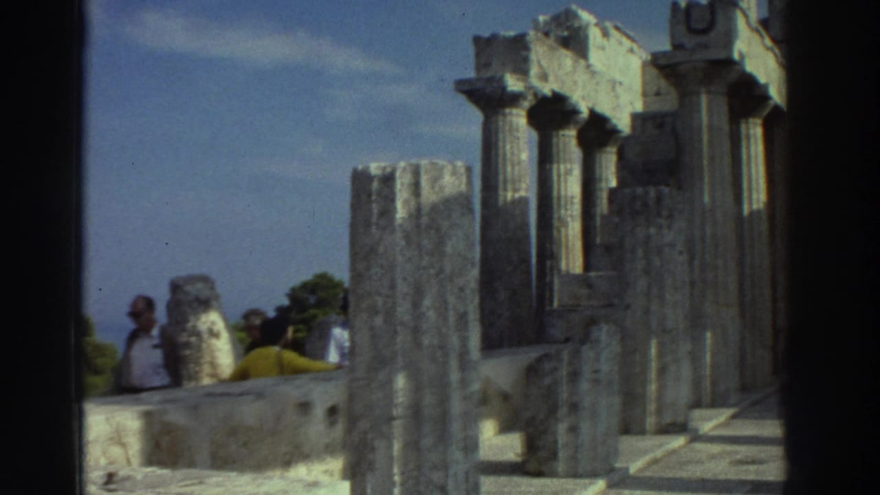 Ancient Greek Doric columns with visitors in light clothing visible among stone ruins against a blue sky