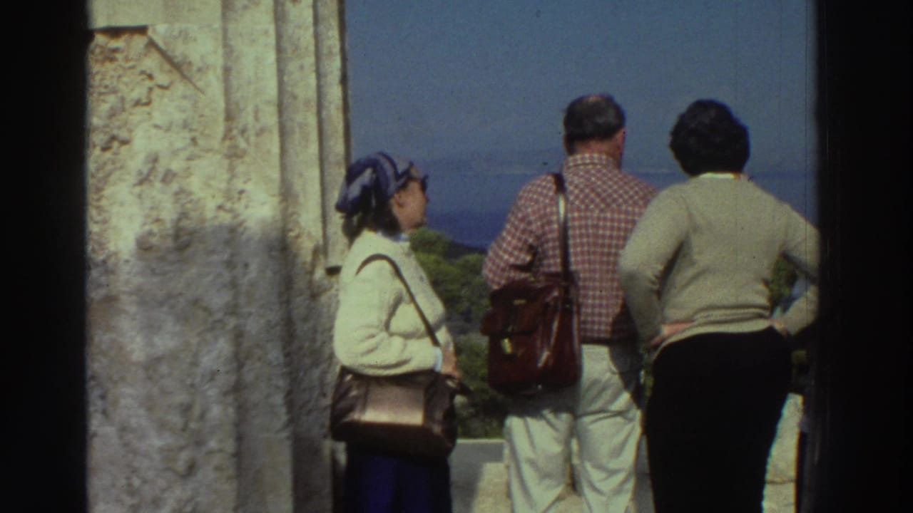 8mm home movie, circa 1976 Greece: group of tourists viewed from behind at an ancient stone overlook, gazing toward a distant blue sea horizon.