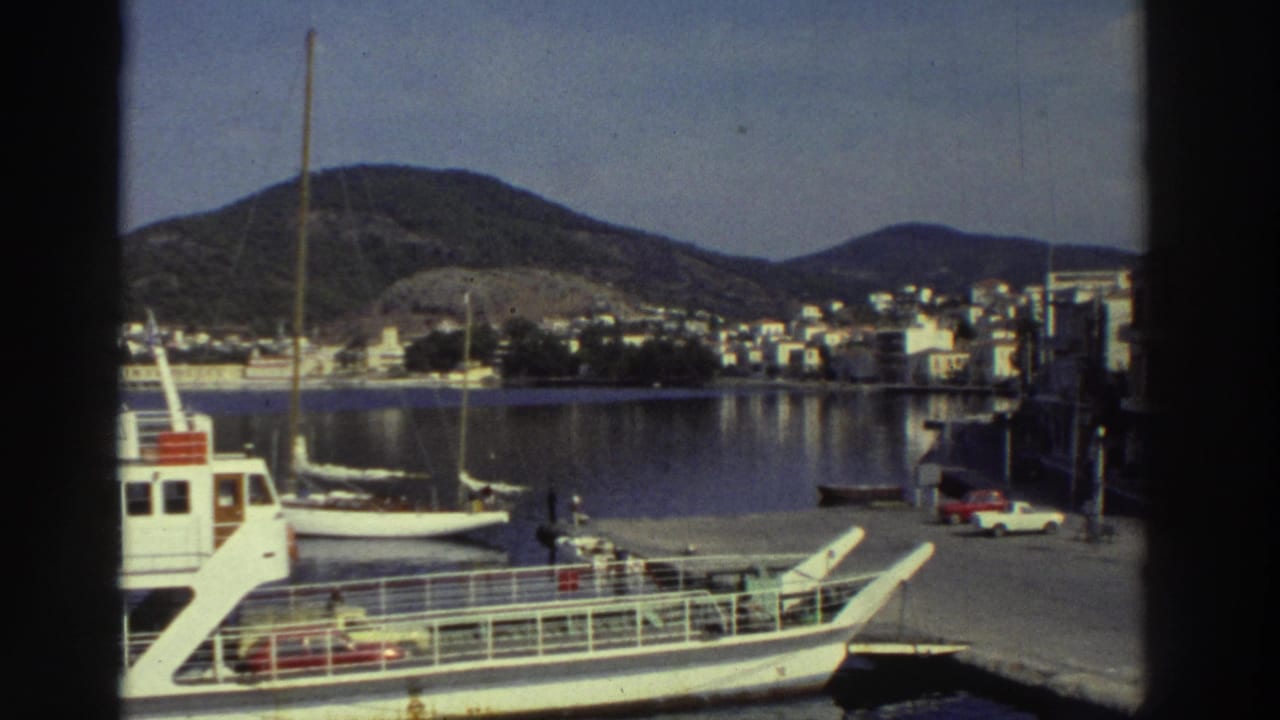 White passenger ferry moored at a quay, with a hillside town of white buildings across the calm harbor.
