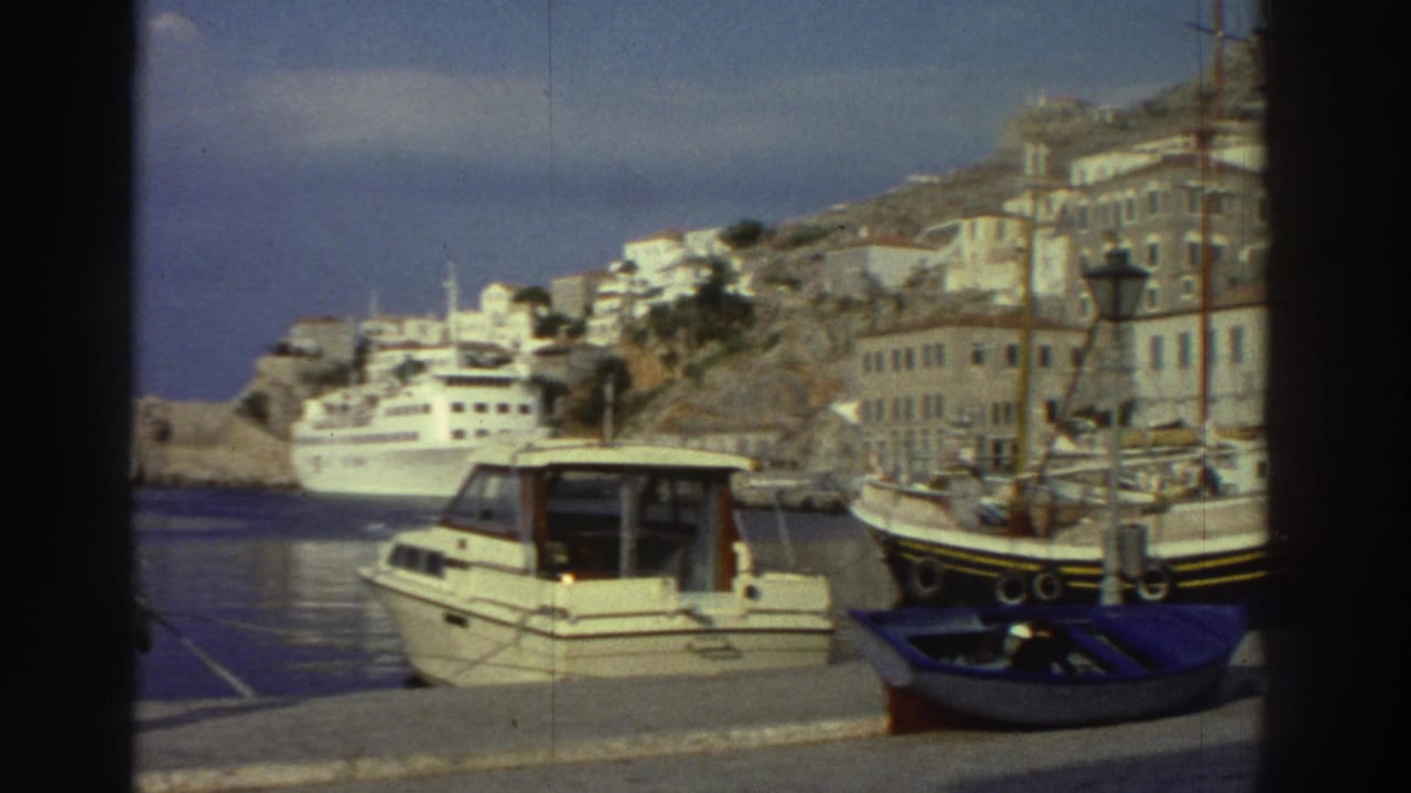 Harbor view through dark vignette: white motorboat and larger fishing vessel moored at a quay, with white hillside buildings and a cruise ship in the background.