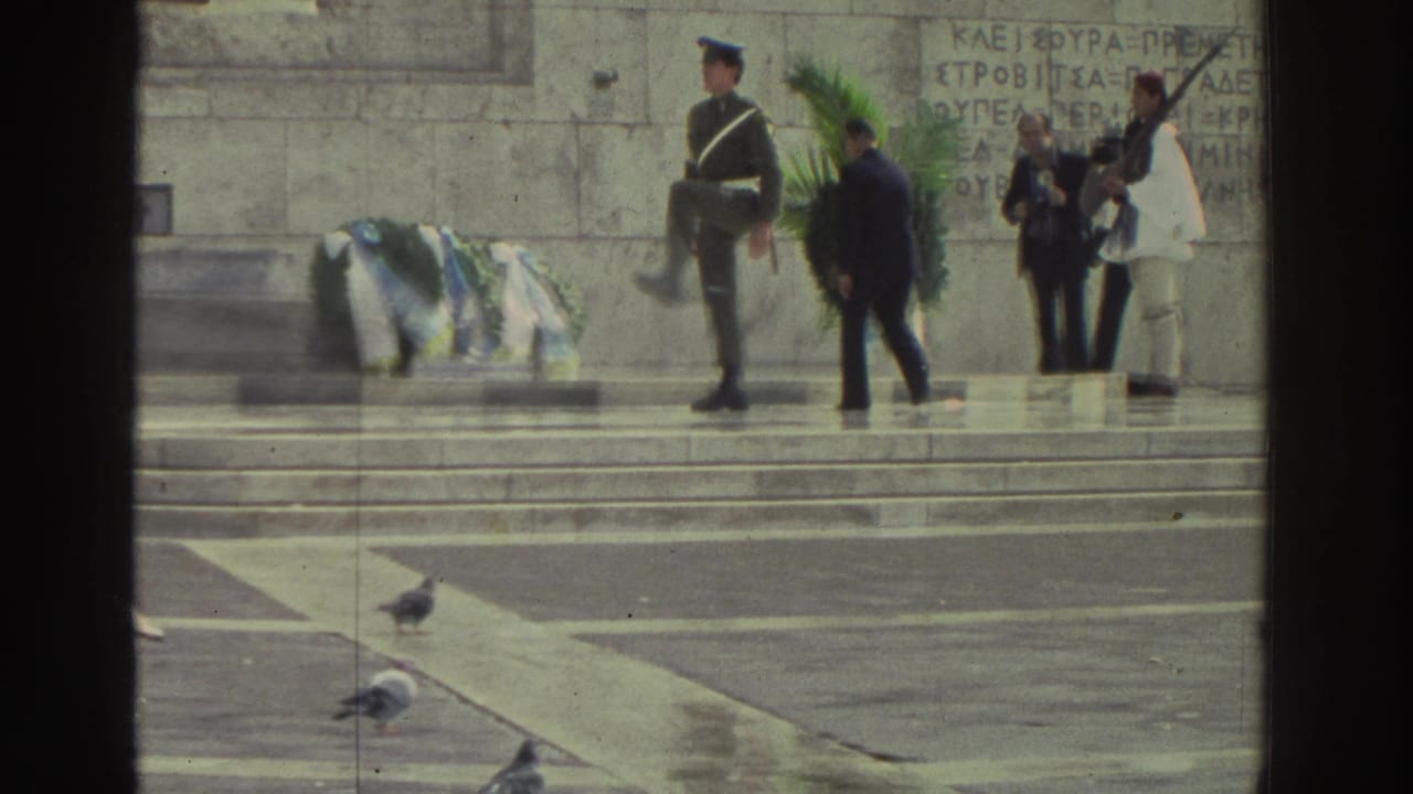 Greek memorial ceremony, circa 1976; ceremonial guard with rifle, civilian and uniformed participants, Evzone-style guards in white; blue-and-white wreaths laid on stone steps, pigeons below.