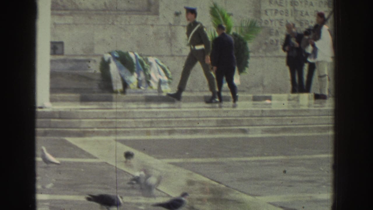 Greece, 1976: soldier in dress uniform walks along stone monument steps during a wreath-laying ceremony; Greek inscriptions carved into the stone wall behind.
