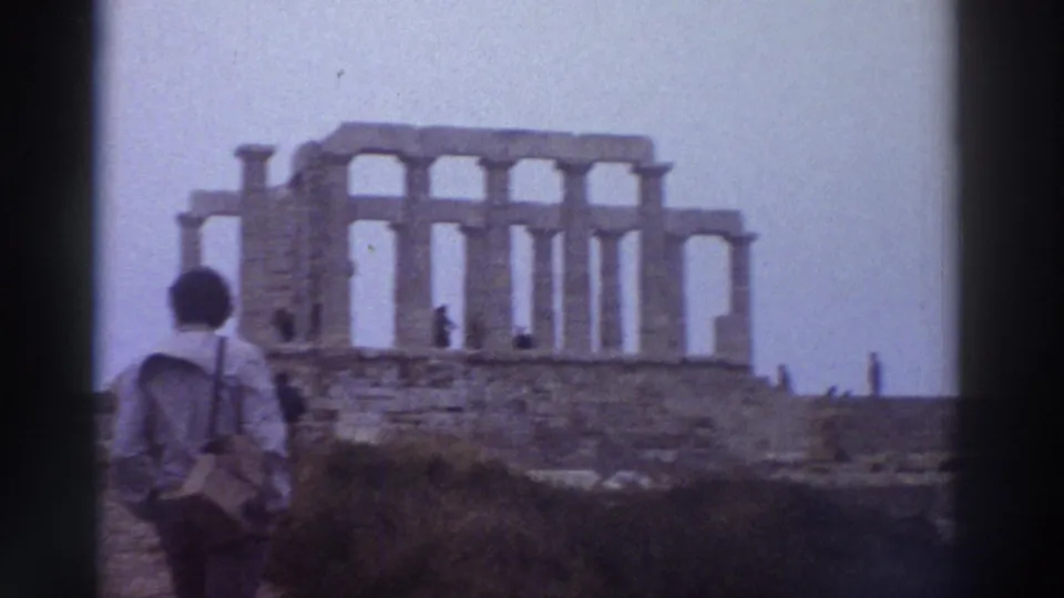 8mm shot of a tourist approaching ancient Doric columns on a hilltop, possibly Cape Sounion area, Greece, circa 1976; hazy overcast sky.