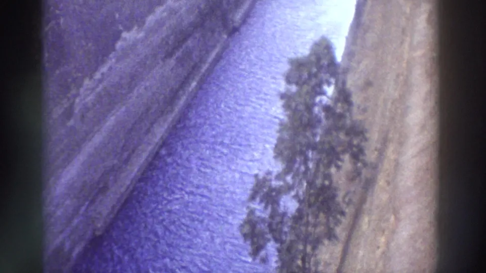 8mm home movie from Greece, c.1976: narrow canal with steep cut-stone walls and blue-toned water, a lone tree at the waterway edge, film grain evident.