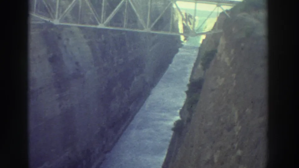1970s 8mm film of a metal truss bridge crossing a narrow canal between steep rock walls, filmed from near bridge level looking down, Greece 1976.