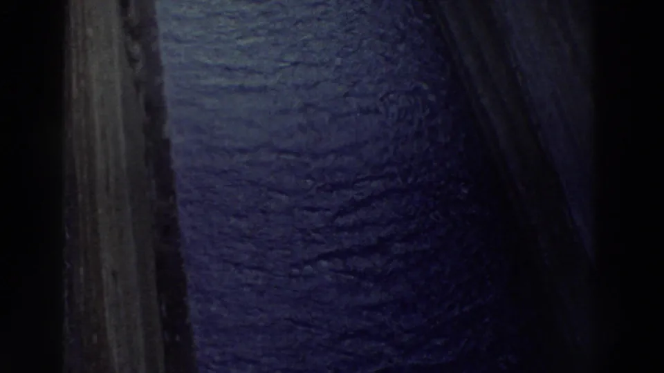 1970s 8mm extreme downward angle over a narrow canal edge showing rippled blue-purple water far below with a limestone cliff face, Greece 1976.