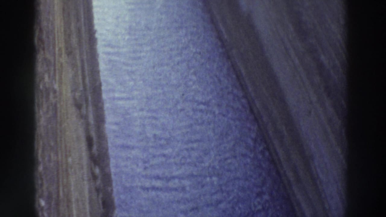 Close-up forward view along a narrow canal, steep stone walls framing blue-purple water
