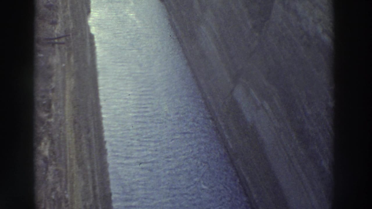 Forward view into narrow canal, grey-blue water between steep stone walls