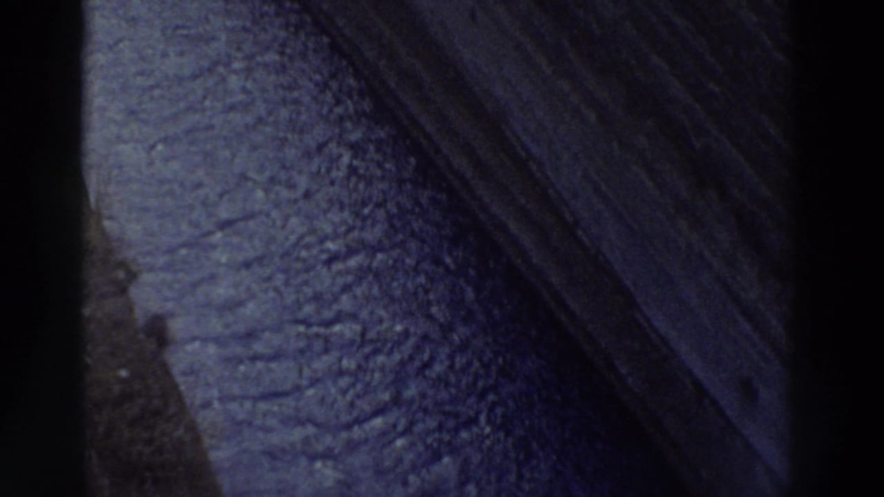 Macro shot of weathered rock surface, diagonal ridge edge cutting across frame, deep blue-purple color cast — 8mm home movie footage, Greece, 1976.