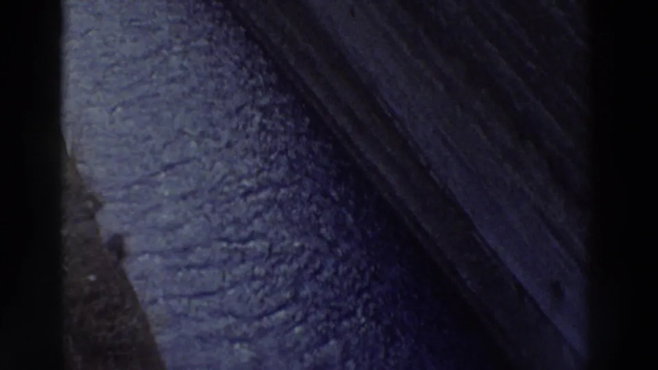 Macro shot of weathered rock surface, diagonal ridge edge cutting across frame, deep blue-purple color cast — 8mm home movie footage, Greece, 1976.