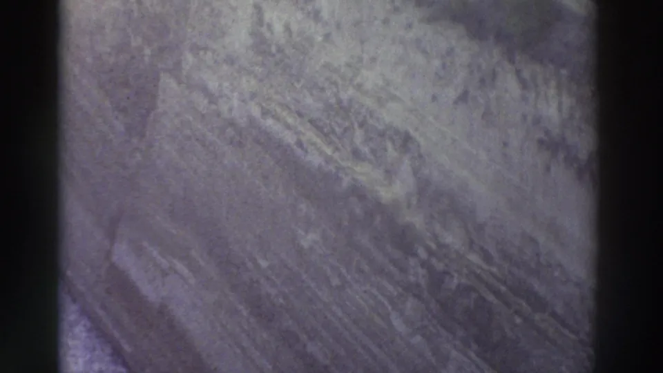 Macro shot of rough terrain surface in muted gray-blue tones, no sky or water visible — 8mm home movie footage, Greece, 1976.