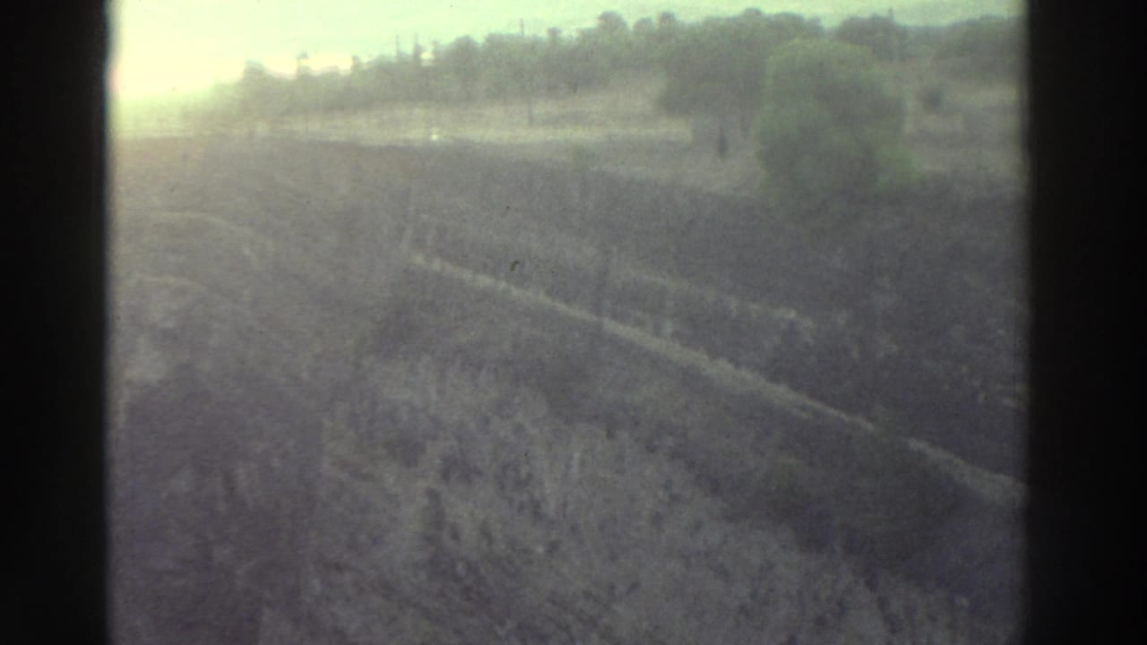 Heavily overexposed Super 8 frame circa 1976 showing a hillside or field with treeline, consistent with a camera roll-in before the ruins sequence.