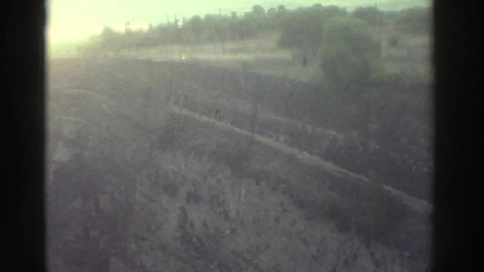 Heavily overexposed Super 8 frame circa 1976 showing a hillside or field with treeline, consistent with a camera roll-in before the ruins sequence.