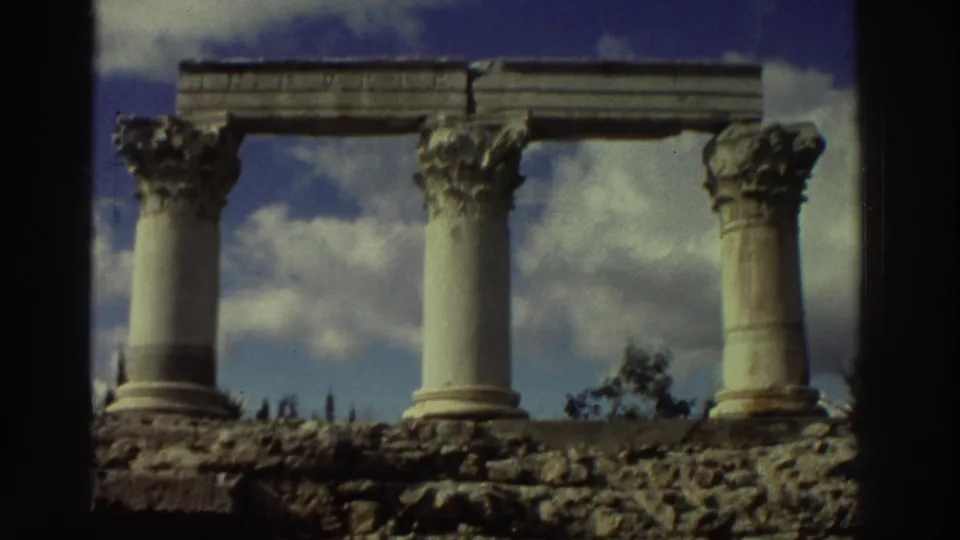 Four Corinthian columns at a Greek archaeological ruin site, circa 1976, shot on 8mm film; partial stone entablature and ruined foundation visible.