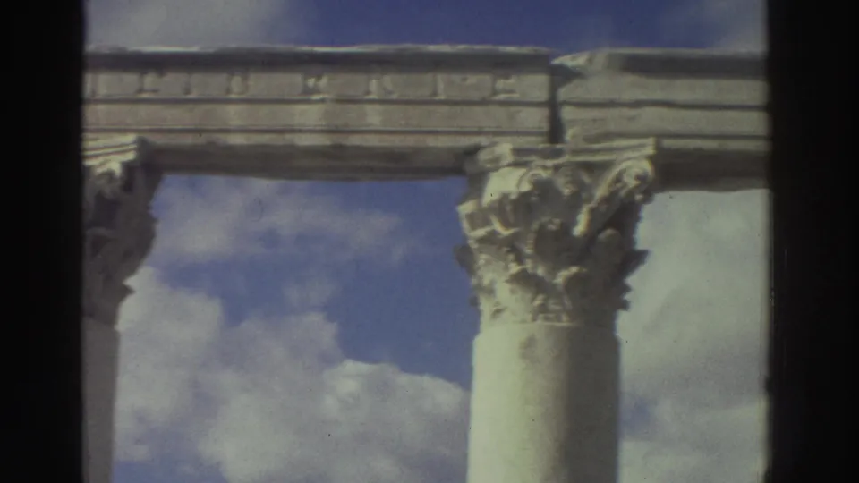Corinthian capital with acanthus leaf carvings beneath an inscribed stone entablature at a Greek ruin, circa 1976, 8mm film.