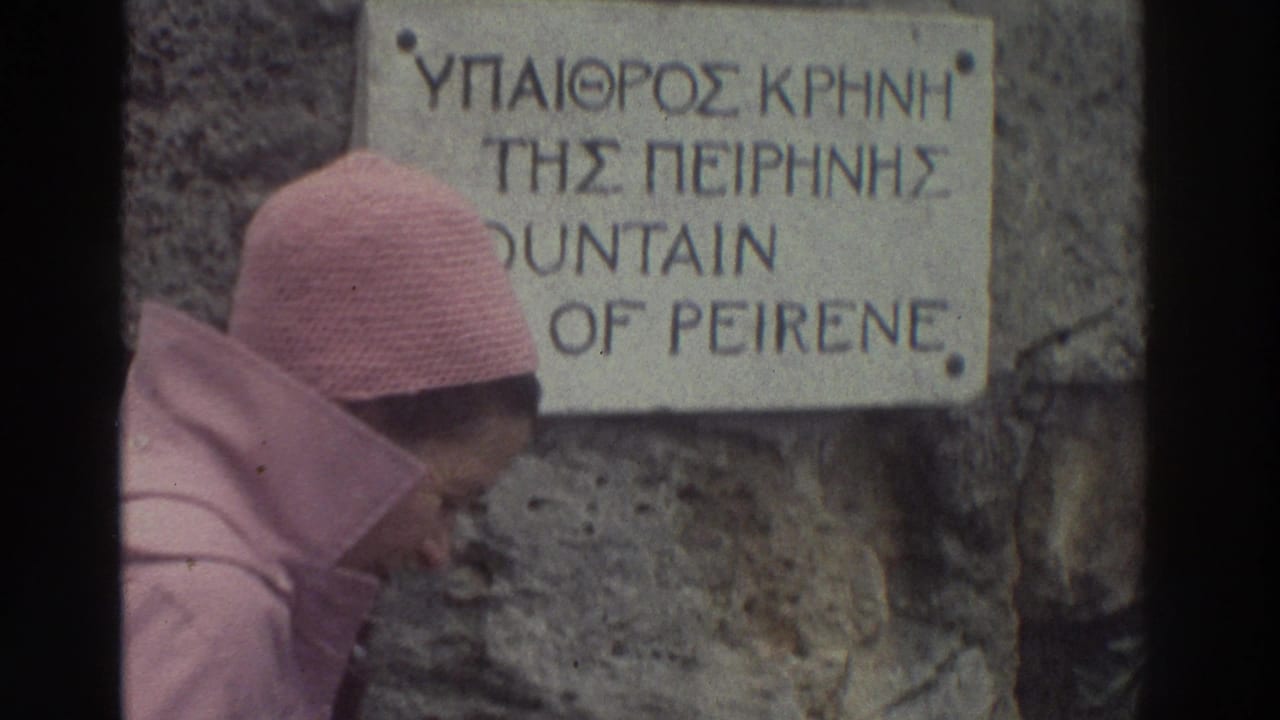 Close-up of a tourist in a pink knitted headscarf beside a carved stone sign reading 'Fountain of Peirene' in Greek and English, Corinth, Greece, c. 1976.