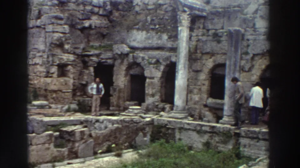 Sparser view of a classical Greek ruin site, c. 1976, showing arched stone niches, standing columns, and a few visitors among the weathered stonework.