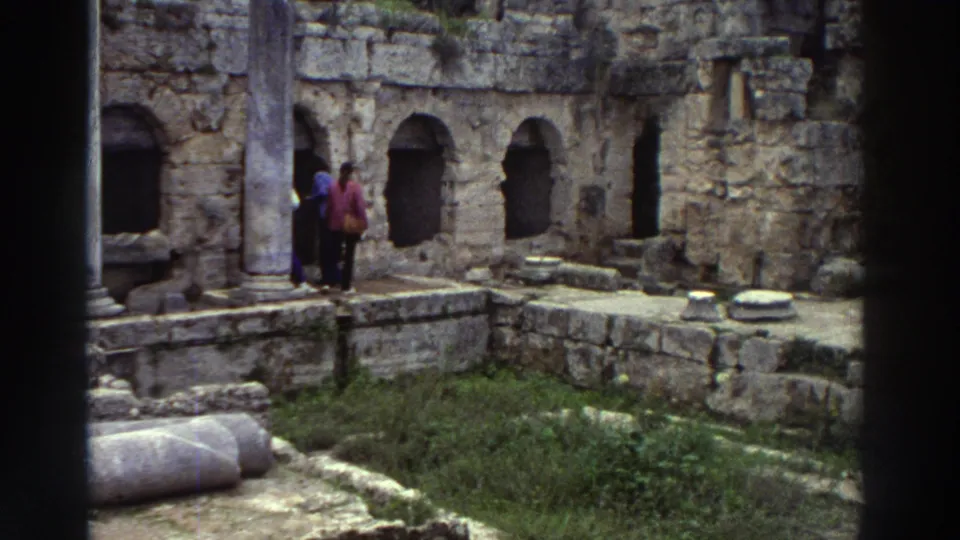 Two tourists in 1970s coats amid ancient stone ruins with arched niches and fallen column drums, Greece, 1976 8mm home movie.
