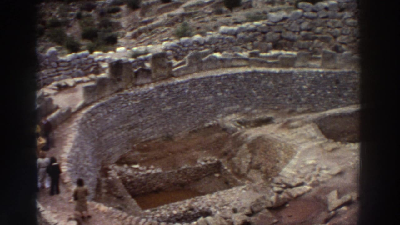 8mm footage from Greece, 1976: elevated view of dry-stone curved ruins on a hillside with one or two small figures visible at lower left.