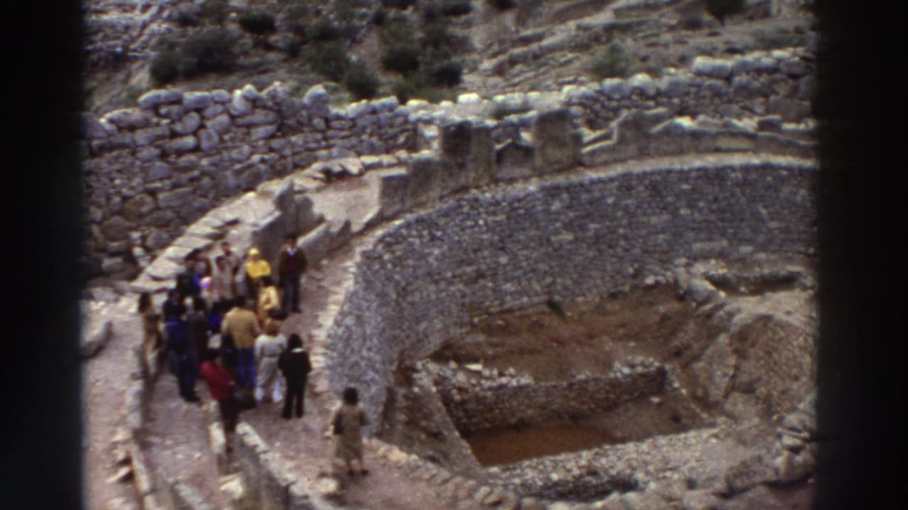 8mm footage from Greece, 1976: approximately a dozen tourists in 1970s casual dress walking through ancient stone ruins along a sunlit stone path.
