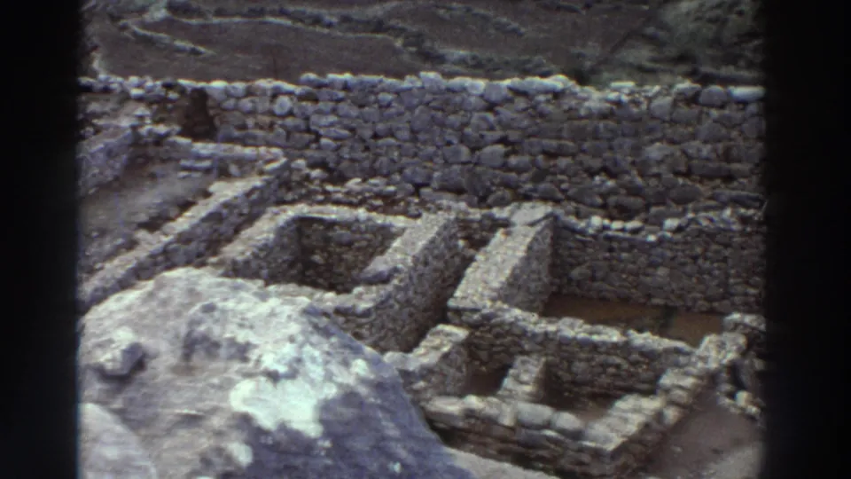 8mm footage from Greece, 1976: close view of multi-room stone ruins with dry-stone construction, exposed soil floors, and hillside beyond.