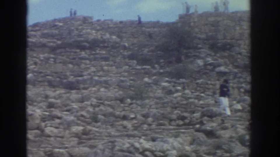 8mm footage of a Greek ancient site, 1976: visitors scattered across rocky ruins and a distant ridge under a pale blue-green sky