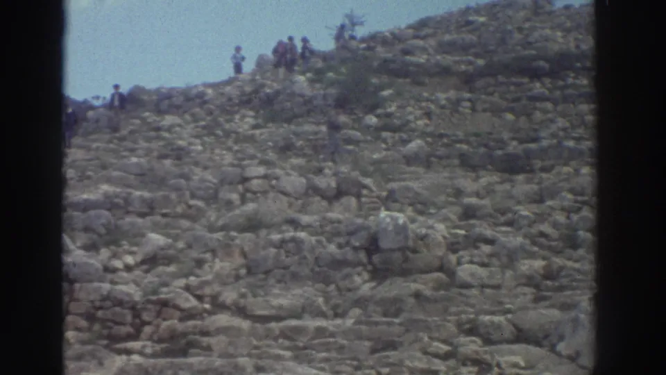 8mm footage of a steep rocky hillside with ancient stone scattered across the slope and visitors near the ridgeline, Greece, 1976
