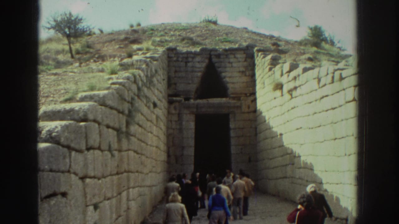 Wider view of tourists approaching a Mycenaean tholos tomb entrance, showing the full height of cyclopean stone walls and the earthen mound above.