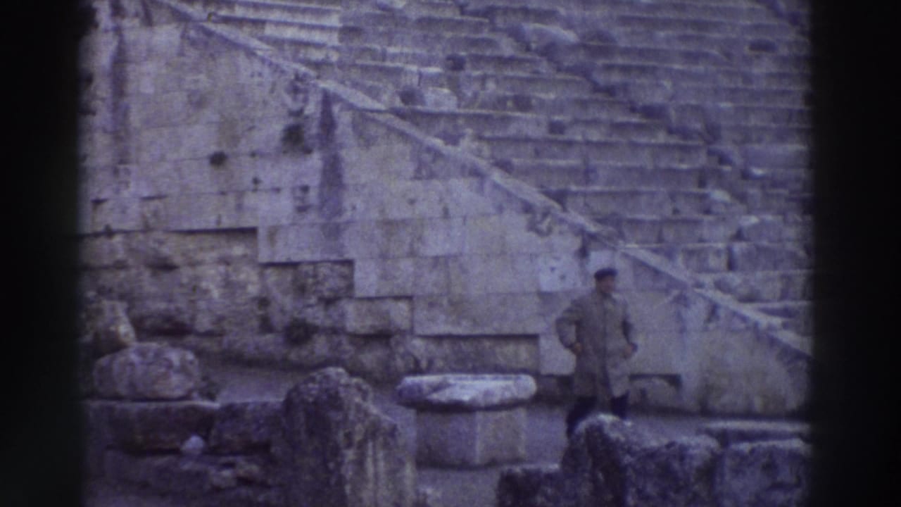 Wide shot of an ancient stone theater's tiered seating rows with a single figure visible on the right side of the steps.
