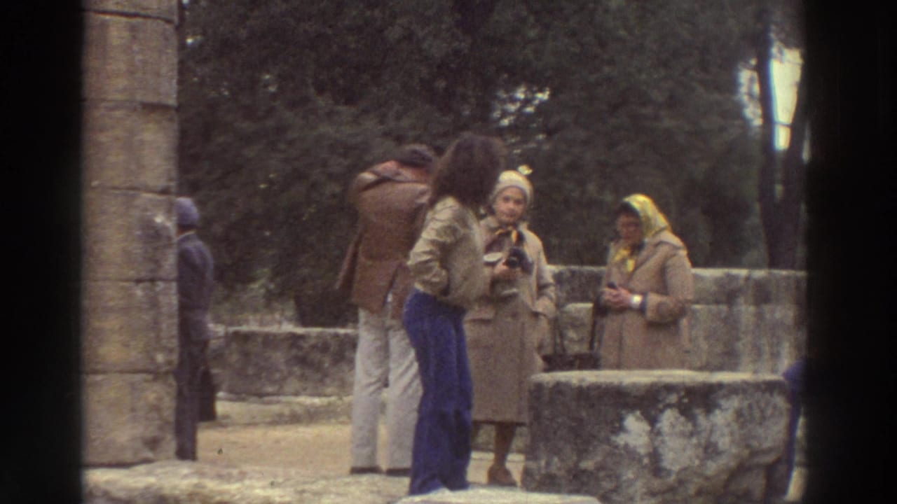 Close group of tourists near a stone column; woman with yellow headscarf and another holding a camera, 1970s dress.